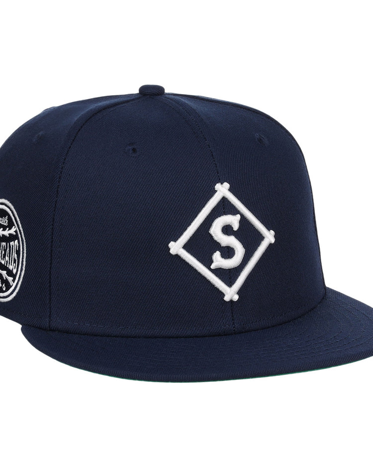 The EFF Seattle Steelheads NLB Team Color Fitted Ballcap is a vintage-inspired navy hat with a white diamond S embroidered logo on the front and a circular patch with text and graphics on the side.