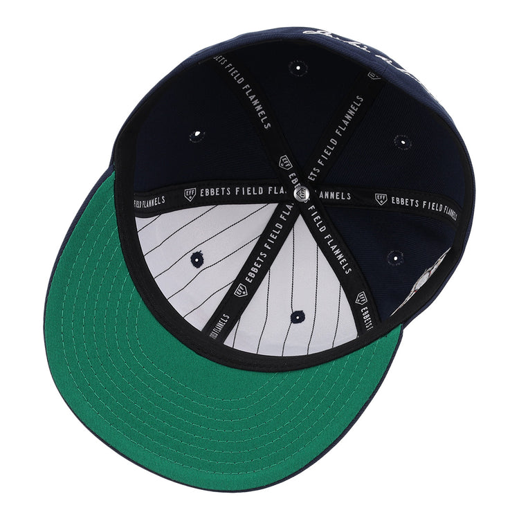 The image shows the underside of the EFF Kansas City Monarchs Robinson Fitted Ballcap in navy, featuring a green brim, navy and white pinstriped inner panels, and black taping labeled EBBETS FIELD FLANNELS for a vintage look.