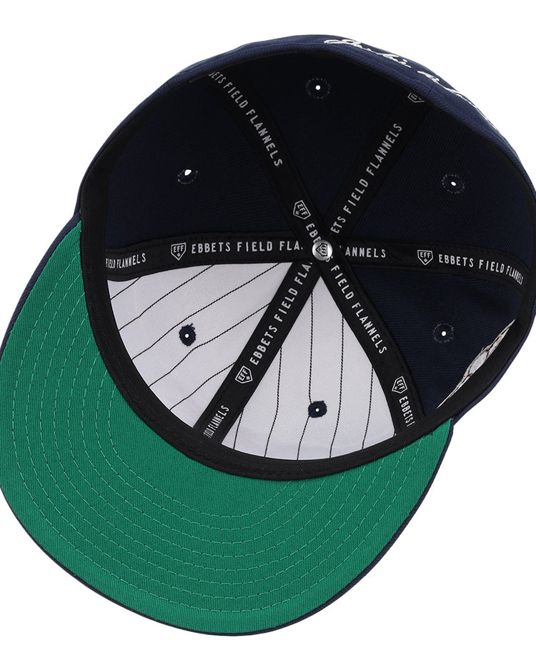 The image shows the underside of the EFF Kansas City Monarchs Robinson Fitted Ballcap in navy, featuring a green brim, navy and white pinstriped inner panels, and black taping labeled EBBETS FIELD FLANNELS for a vintage look.