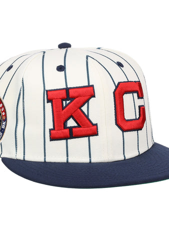 The EFF Kansas City Monarchs Robinson Pinstripe Fitted Ballcap features a white design with navy pinstripes, a navy brim, bold red embroidered KC logo on the front, and a commemorative side patch.