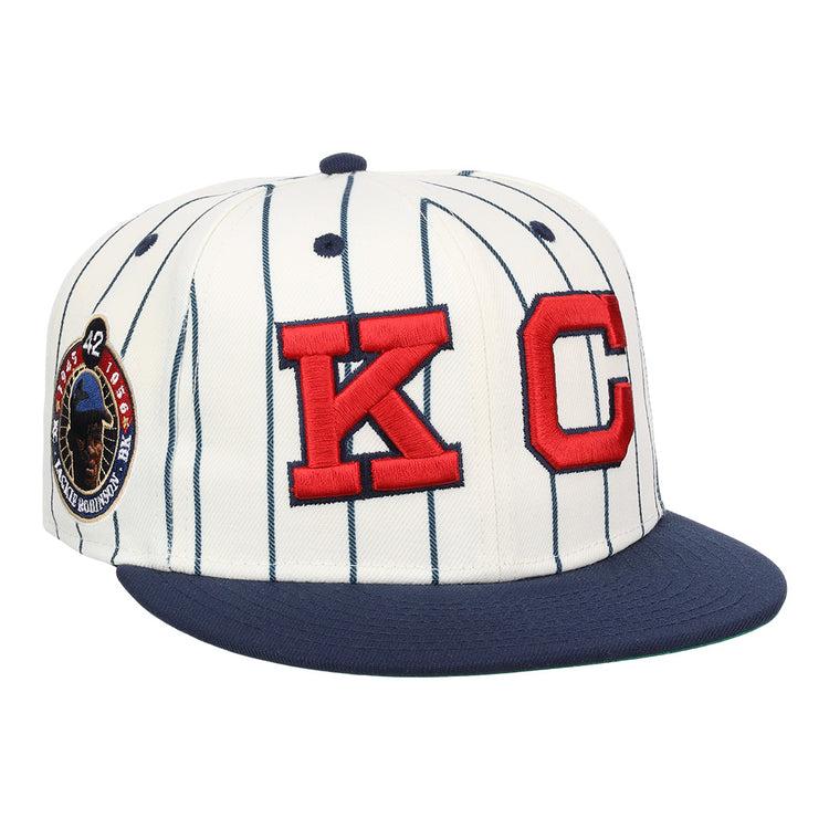 The EFF Kansas City Monarchs Robinson Pinstripe Fitted Ballcap features a white design with navy pinstripes, a navy brim, bold red embroidered KC logo on the front, and a commemorative side patch.