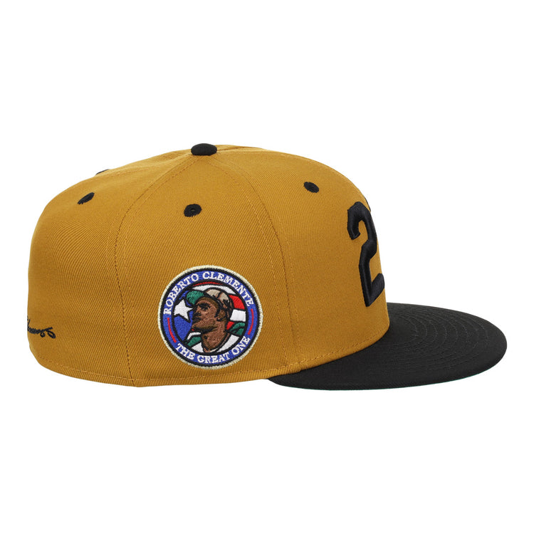 The EFF Roberto Clemente Signature Series Fitted Ballcap in gold features black accents, a 21 on the side, and a patch with Clemente’s portrait, name, and The Great One.