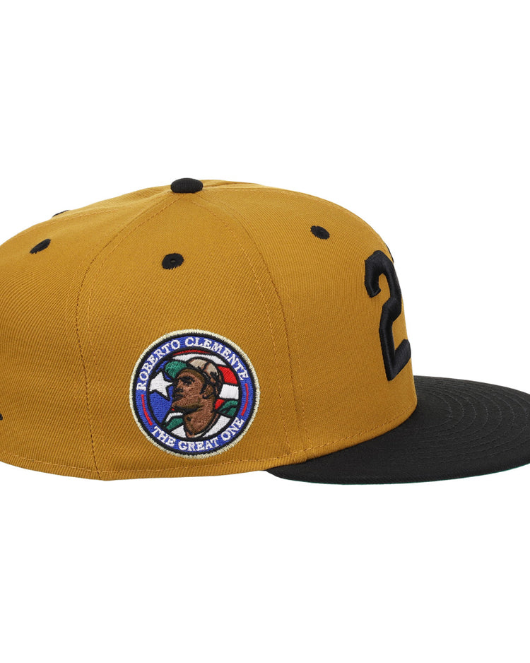 The EFF Roberto Clemente Signature Series Fitted Ballcap in gold features black accents, a 21 on the side, and a patch with Clemente’s portrait, name, and The Great One.