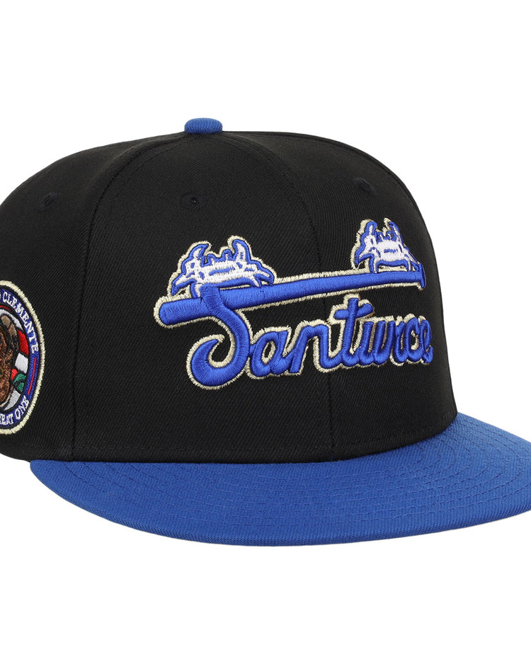 The EFF Santurce Cangrejeros Clemente Fitted Ballcap in black features a blue brim, Santurce embroidered in blue and white, and a side patch honoring Puerto Rican baseball legend Roberto Clemente with Campeón Caribe 1951.