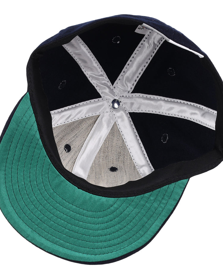 The image shows the inside of the Carta Blanca 1939 Vintage Ballcap by Ebbets Field Flannels, featuring a green underbrim, black sweatband, silver lining strips, and embroidered eyelets inspired by a classic Mexican League design.