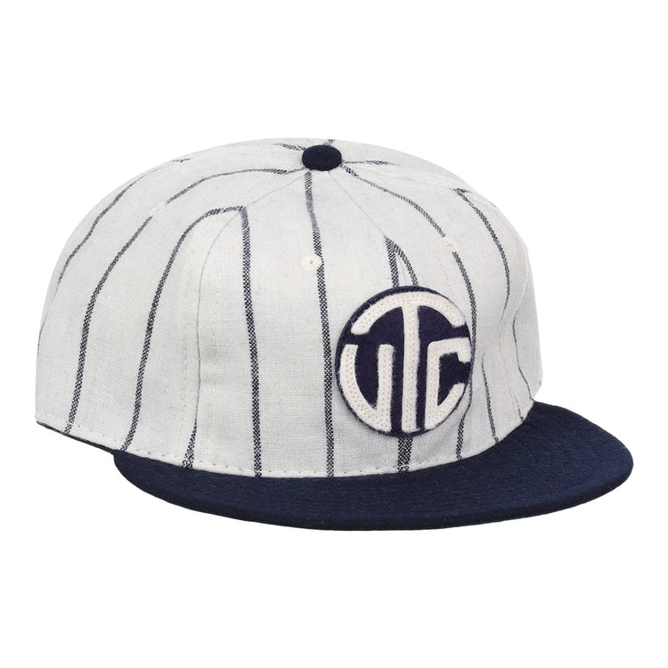 The Vedado TC 1930 Vintage Ballcap by Ebbets Field Flannels features thin vertical navy stripes, a navy brim, and a circular front patch with bold white UTC letters on navy, inspired by the classic Vedado TC ballcap.