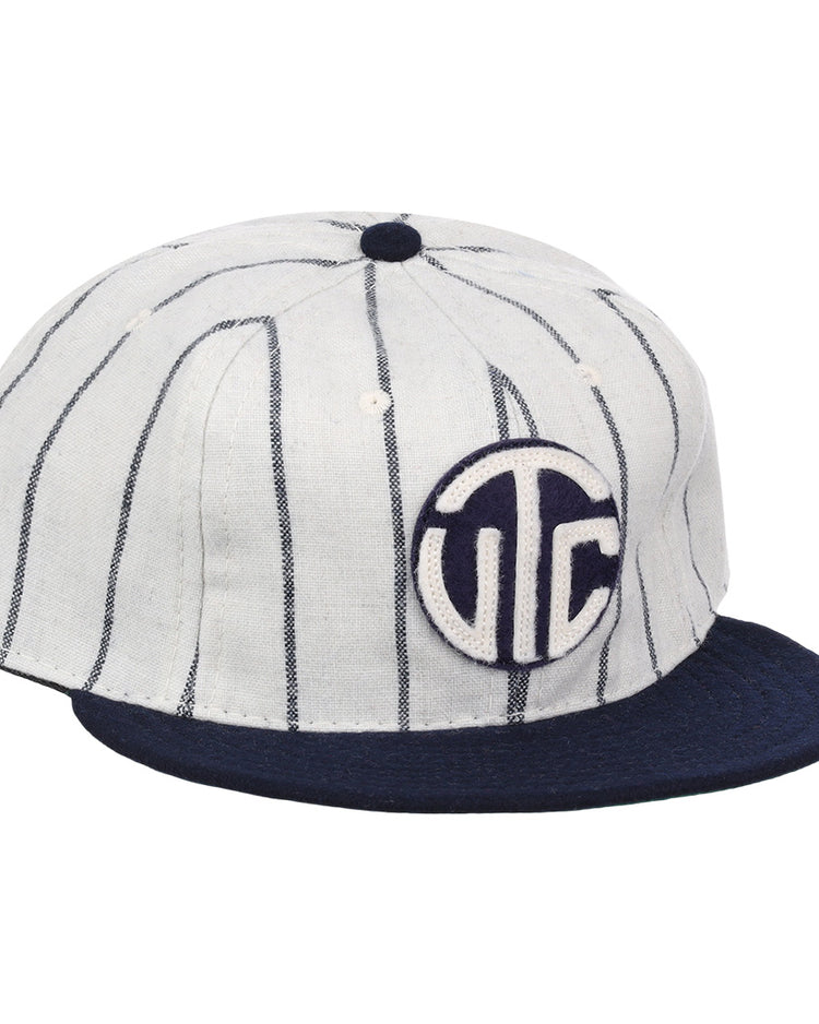 The Vedado TC 1930 Vintage Ballcap by Ebbets Field Flannels features thin vertical navy stripes, a navy brim, and a circular front patch with bold white UTC letters on navy, inspired by the classic Vedado TC ballcap.