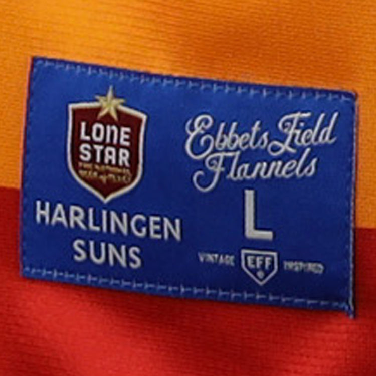 A blue label on orange and red fabric reads “EFF” and “Harlingen Suns,” featuring the Harlingen Suns EFF Lone Star Baseball Jersey by EFF, with vintage details honoring Texas baseball and the Lone Star League.