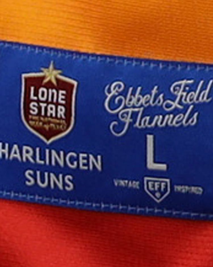 A blue label on orange and red fabric reads “EFF” and “Harlingen Suns,” featuring the Harlingen Suns EFF Lone Star Baseball Jersey by EFF, with vintage details honoring Texas baseball and the Lone Star League.