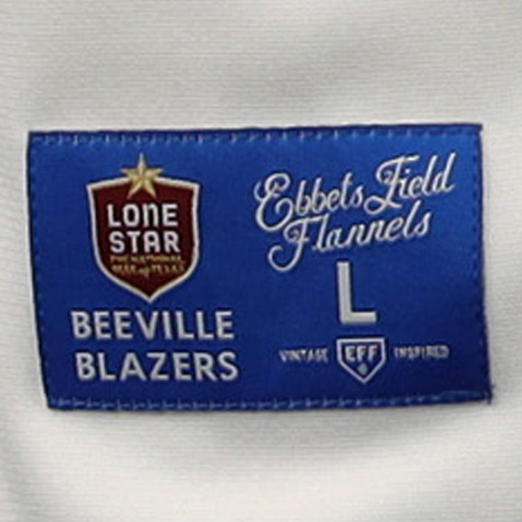 The blue and white fabric label on the Beeville Blazers EFF Lone Star Baseball Jersey (by EFF) features various logos, decorative fonts, and text including Beeville Blazers, Joe Hunter Field, L, and Vintage EFF Inspired.