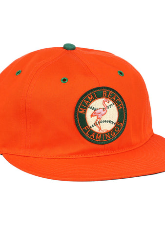 The EFF Miami Beach Flamingos Cotton Twill Ballcap is an orange cap with a circular green and yellow flamingos patch, Miami Beach Flamingos text, green eyelets and top accents, flat brim, and adjustable leather strap.