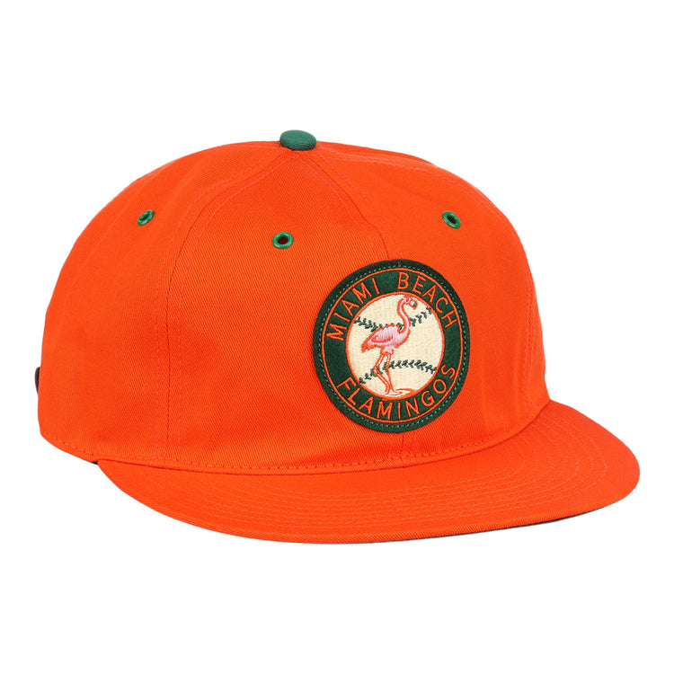 The EFF Miami Beach Flamingos Cotton Twill Ballcap is an orange cap with a circular green and yellow flamingos patch, Miami Beach Flamingos text, green eyelets and top accents, flat brim, and adjustable leather strap.
