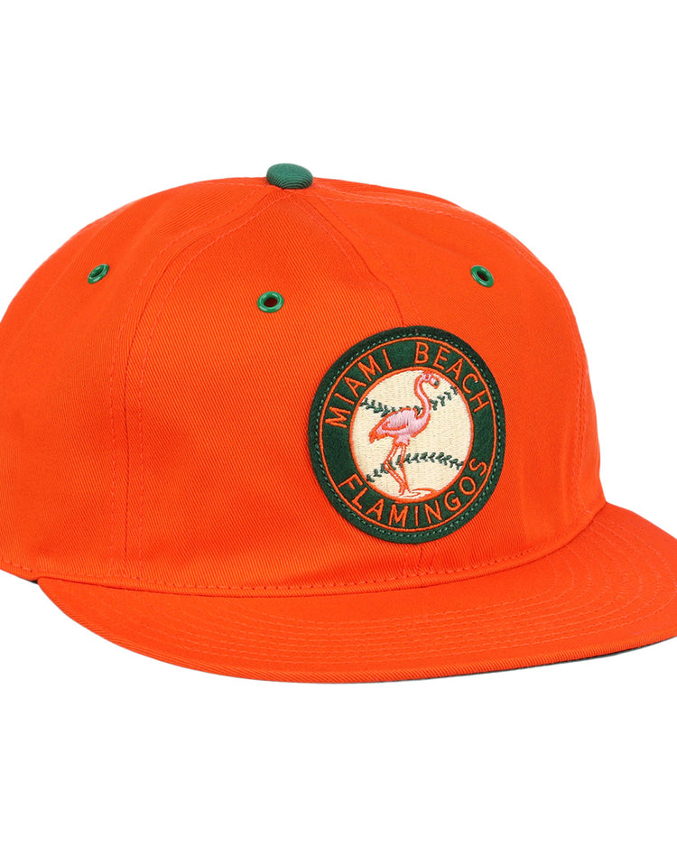 The EFF Miami Beach Flamingos Cotton Twill Ballcap is an orange cap with a circular green and yellow flamingos patch, Miami Beach Flamingos text, green eyelets and top accents, flat brim, and adjustable leather strap.