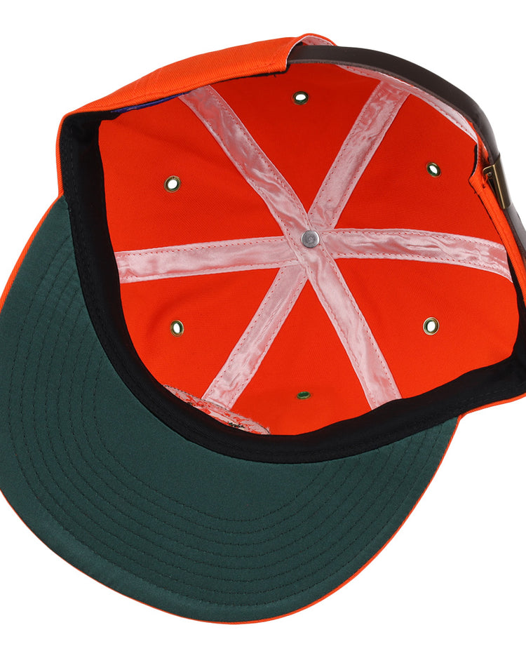 The image shows the inside of an EFF Miami Beach Flamingos Cotton Twill Ballcap, featuring orange cotton fabric, a green underbrim, white sweatbands in an X shape, and an adjustable leather strap at the back.