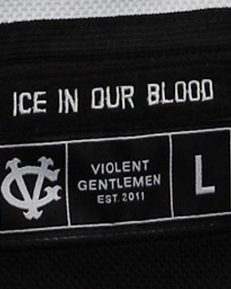 Close-up of a black clothing label on the Violent Gentlemen x EFF Collection Hockey Jersey by EFF, reading ICE IN OUR BLOOD and VIOLENT GENTLEMEN EST.2011, with a white symbol and size L shown.