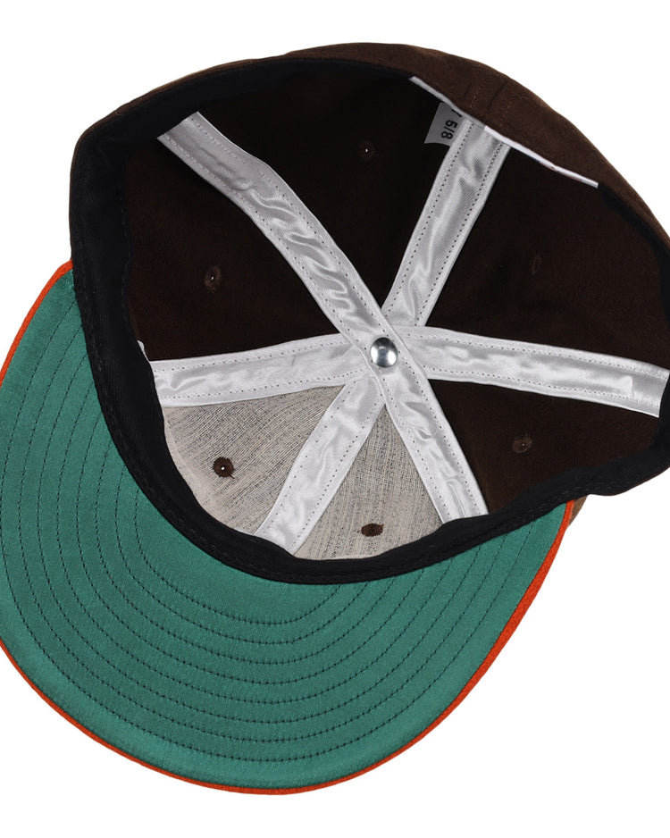 The image shows the inside of an EFF Pine Bluff Judges 1953 Vintage Ballcap, featuring a green brim with orange edge, brown panels, white cross-shaped stitching, and a silver button.