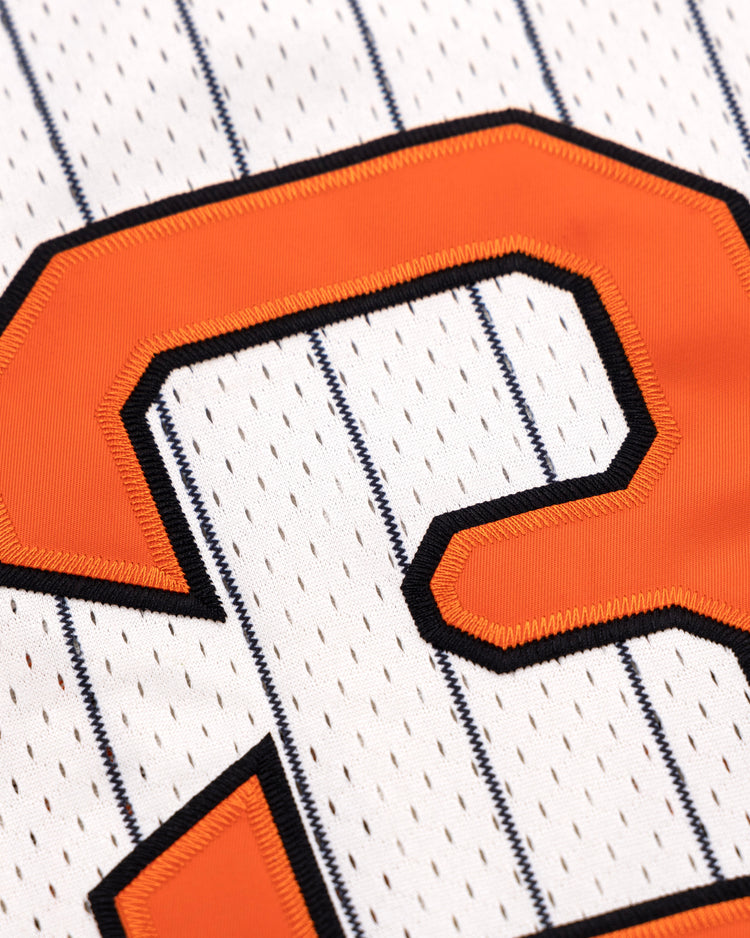 Close-up of an orange number 3 with a black outline stitched onto a white EFF Sioux City Ghosts Pinstripe Button Down Jersey, featuring thin vertical navy blue pinstripes.