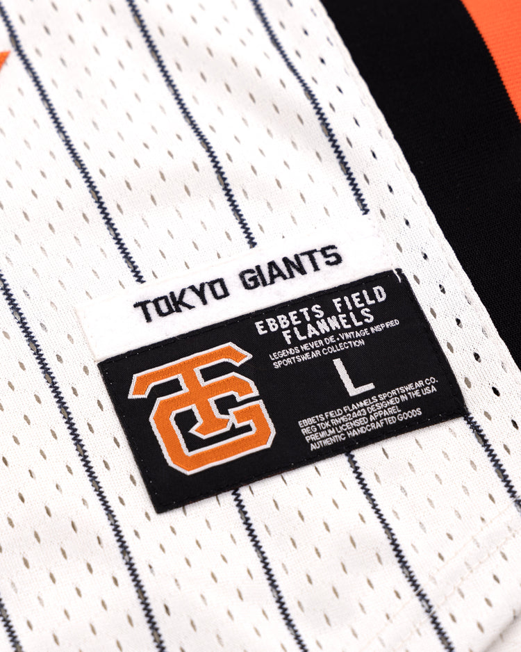 Close-up of the Tokyo Giants EFF Pinstripe Button Down Jersey by EFF, featuring black pinstripes on white fabric and two labels: one with TOKYO GIANTS and another displaying a large orange and black logo plus EBBETS FIELD FLANNELS.