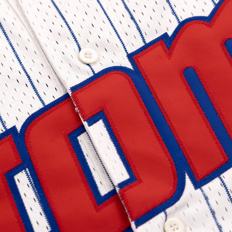 Close-up of the Sankei Atoms EFF Pinstripe Button Down Jersey by EFF: white fabric with thin blue pinstripes, blue trim, white buttons, and large partially visible red and blue lettering across the chest.