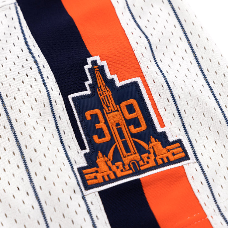 Close-up of the San Francisco Seals EFF Pinstripe Button Down Jersey by EFF, with white fabric, black pinstripes, a patch showing the number 39 and a stylized cityscape in orange and navy, plus an orange and navy vertical stripe behind the patch.