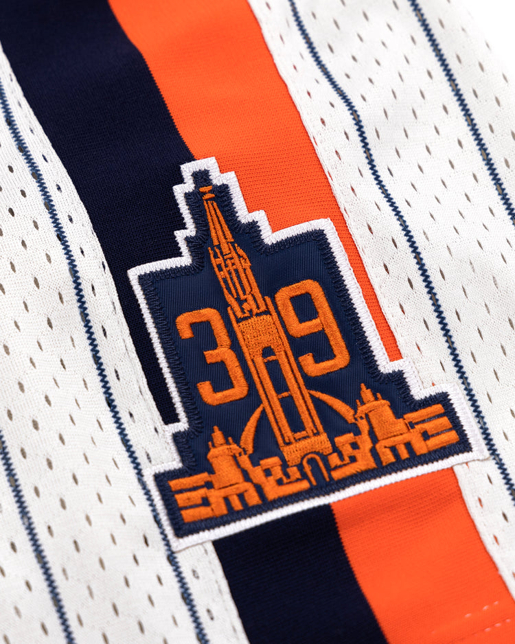 Close-up of the San Francisco Seals EFF Pinstripe Button Down Jersey by EFF, with white fabric, black pinstripes, a patch showing the number 39 and a stylized cityscape in orange and navy, plus an orange and navy vertical stripe behind the patch.
