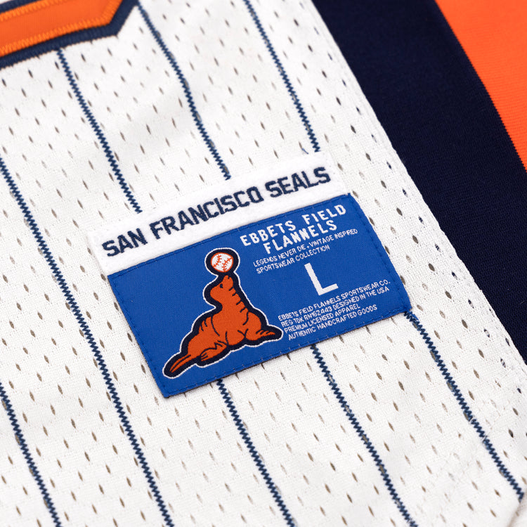 A close-up of the EFF San Francisco Seals Pinstripe Button Down Jersey label, showing a blue tag with orange seal logo, size L, and EFF branding on a white pinstripe jersey with blue accents and navy/orange trim.