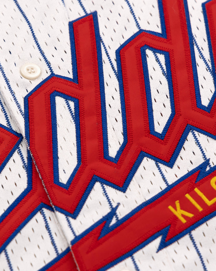 Close-up of the EFF Reddy Kilowatt EFF Pinstripe Button Down Jersey, a white pinstripe baseball jersey with bold red and blue lettering and KILOW in yellow on a red background.