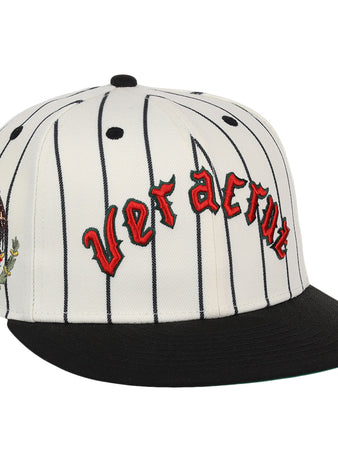 The Veracruz NLB Pinstripe Fitted Ballcap by EFF is a white cap with black pinstripes, a black brim, Veracruz in red gothic letters on the front, and an eagle-and-cactus embroidered patch on the side.
