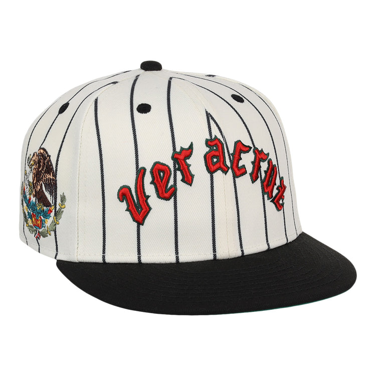 The Veracruz NLB Pinstripe Fitted Ballcap by EFF is a white cap with black pinstripes, a black brim, Veracruz in red gothic letters on the front, and an eagle-and-cactus embroidered patch on the side.