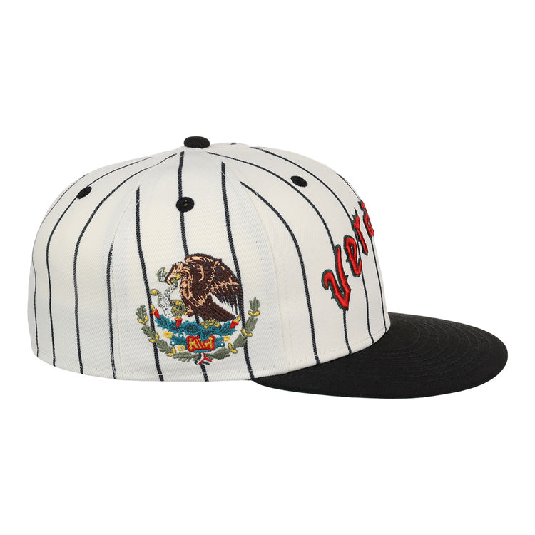 The EFF Veracruz NLB Pinstripe Fitted Ballcap features white fabric with black pinstripes, a black brim, side embroidery of the Mexican coat of arms, and partially visible red letters on the front.