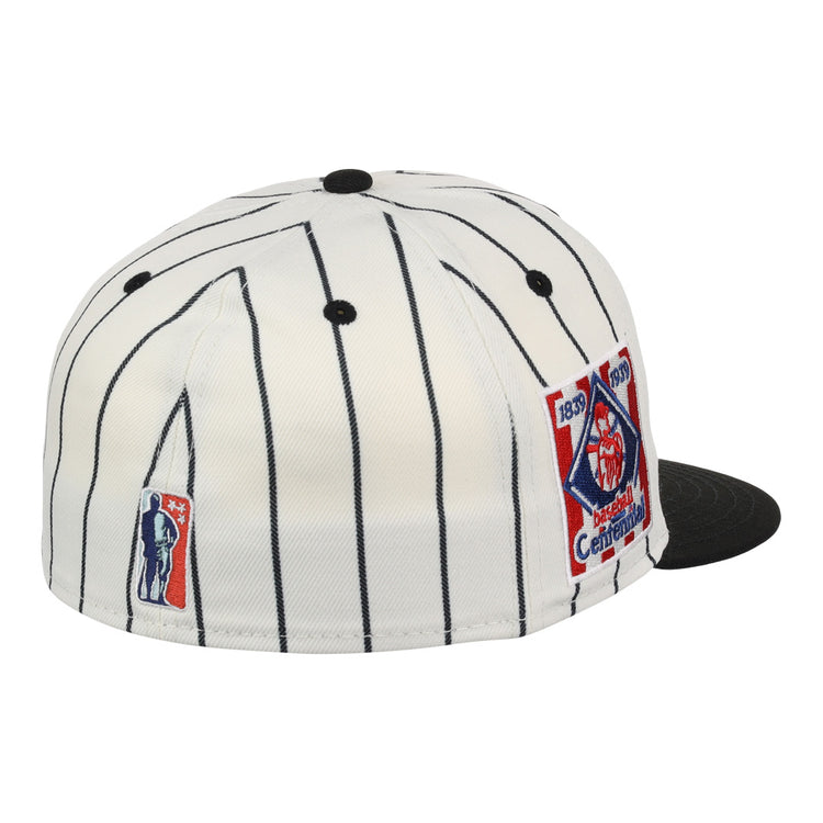 The EFF Philadelphia Stars NLB Pinstripe Fitted Ballcap is a white cap with black pinstripes, a black brim, and two embroidered patches—one for the Negro National League centennial and one with a batter’s silhouette.