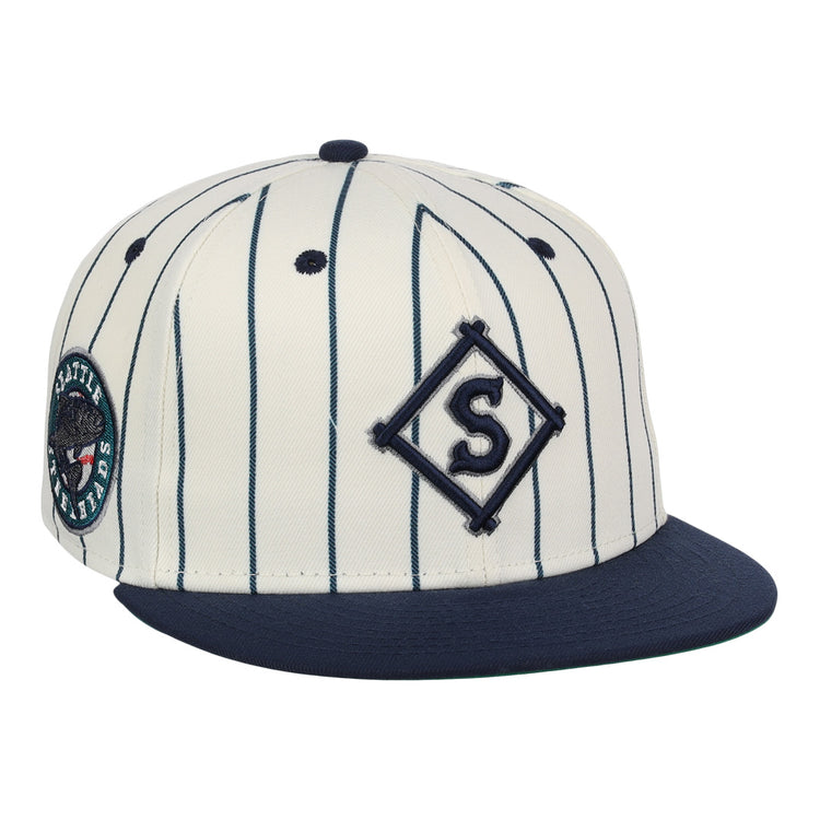 The EFF Seattle Steelheads NLB Pinstripe Fitted Ballcap features a cream base with navy pinstripes, a navy bill, an embroidered S in a diamond on the front, and a Seattle Mariners patch on the side.