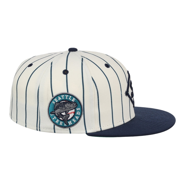 The EFF Seattle Steelheads NLB Pinstripe Fitted Ballcap features white fabric with navy pinstripes, a navy brim, and a round side patch reading Seattle Fish Heads with a fish graphic, inspired by the NLB Pinstripe Collection.