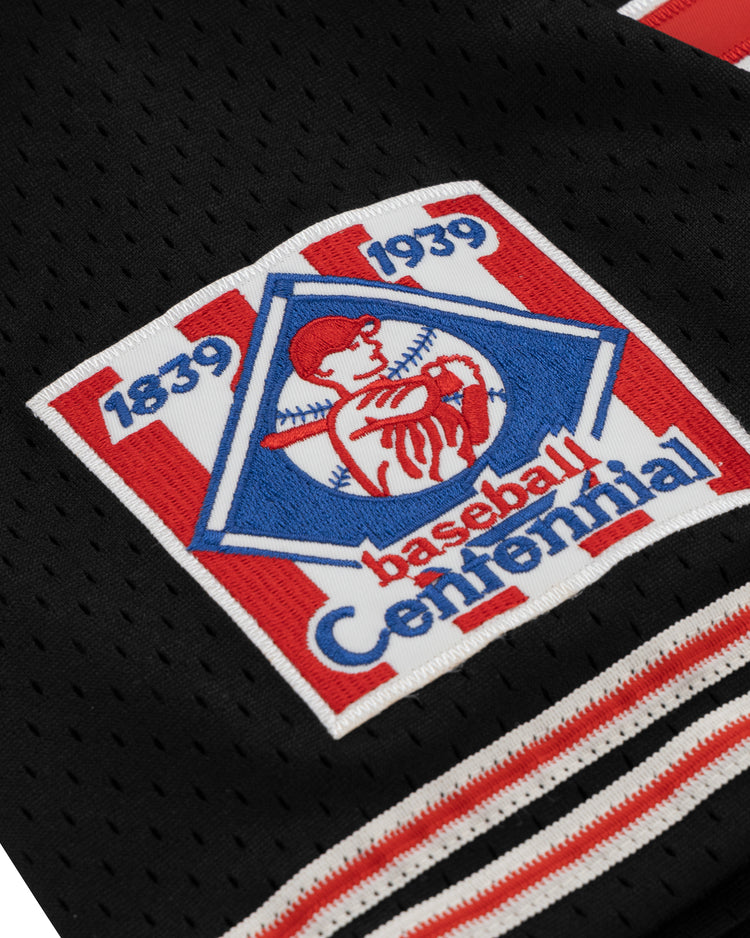 A close-up of the EFF Cultural Excellence x Philadelphia Stars Button Down Jersey, a black sports jersey inspired by Negro League Baseball, featuring a red, white, and blue 1839–1939 Baseball Centennial patch with a batter in a pentagon.