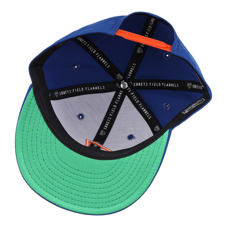 The Jacksonville Suns EFF MiLB Vintage Snapback by Ebbets Field Flannels features a blue cap, green undervisor, black seams with branded text, orange sweatband accents, and an embroidered J logo from the Vintage Minor League collection.