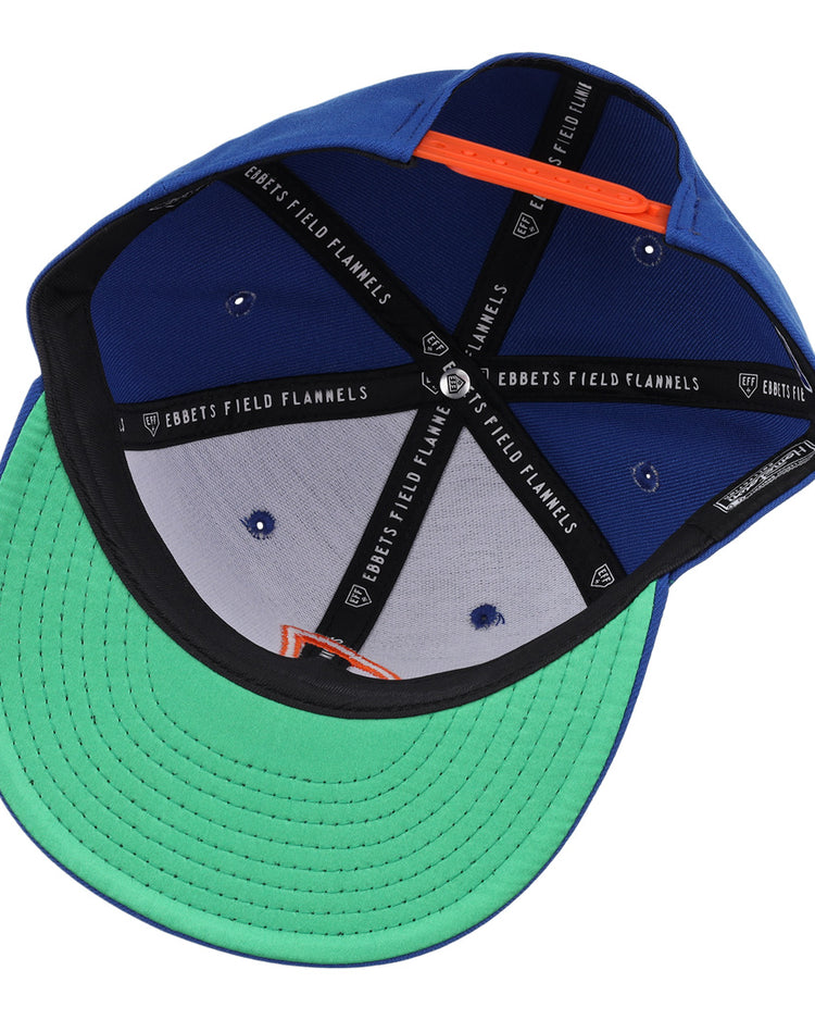 The Jacksonville Suns EFF MiLB Vintage Snapback by Ebbets Field Flannels features a blue cap, green undervisor, black seams with branded text, orange sweatband accents, and an embroidered J logo from the Vintage Minor League collection.
