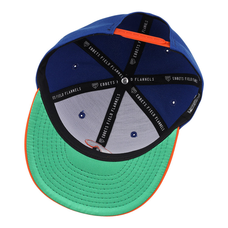 The Charlotte Orioles EFF MiLB Vintage Snapback by Ebbets Field Flannels features a blue crown, green brim, orange trim, and black interior taping—reflecting classic stitching and structure from Cal Ripken Jr.’s early career.