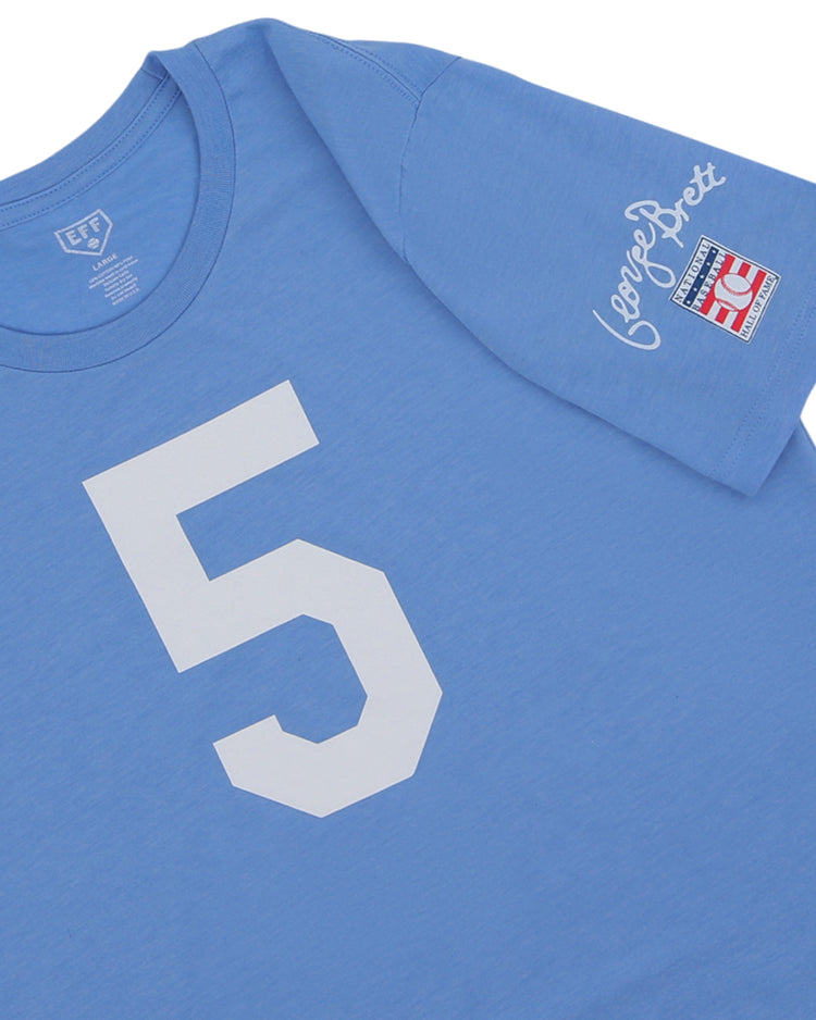 The George Brett Hall of Fame T-Shirt by Ebbets Field Flannels features a light blue design, large white number 5 on the front, and a sleeve patch with red and blue details plus George Brett’s cursive signature.