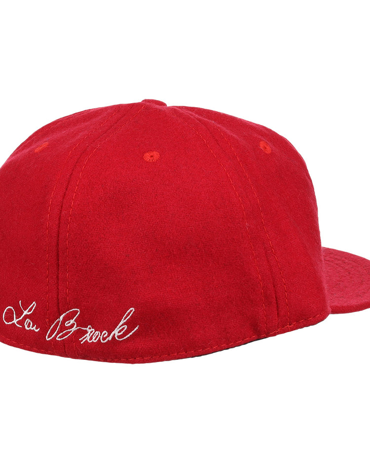 The Ebbets Field Flannels Lou Brock Signature Series Ballcap is a vintage red wool cap, shown from the back left, with Lou Brock’s signature in white cursive embroidered above the band.
