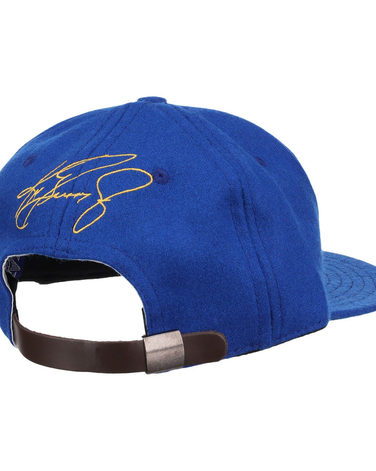 Shown from the back, the Ken Griffey Jr. 1989 Signature Series Ballcap by Ebbets Field Flannels features blue vintage wool, an adjustable brown strap with metal clasp, and a yellow signature embroidered on the top left side—ideal for collectors.