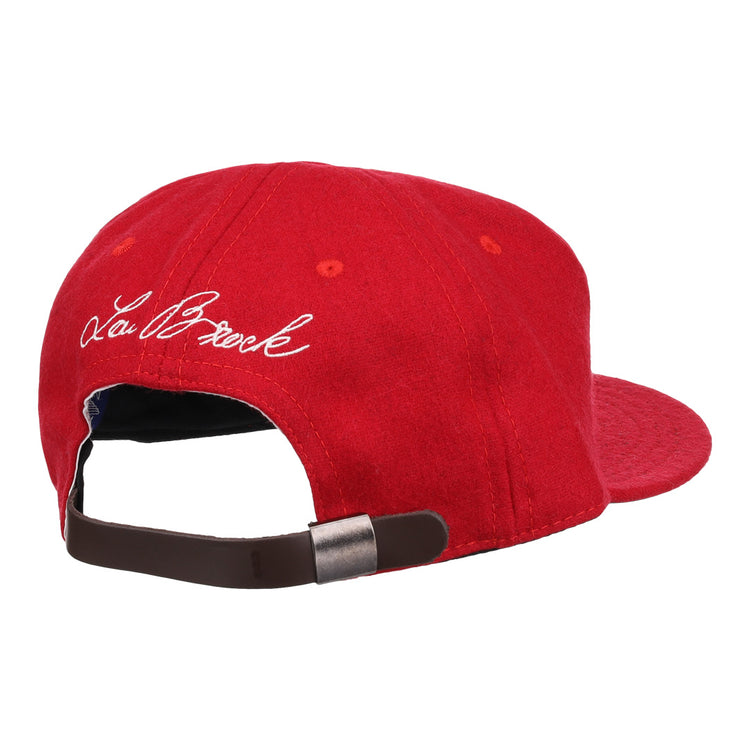 The Ebbets Field Flannels Lou Brock Signature Series Ballcap is a red vintage wool cap with a brown adjustable strap and metal clasp. White cursive embroidery of the Lou Brock signature appears on the left side.