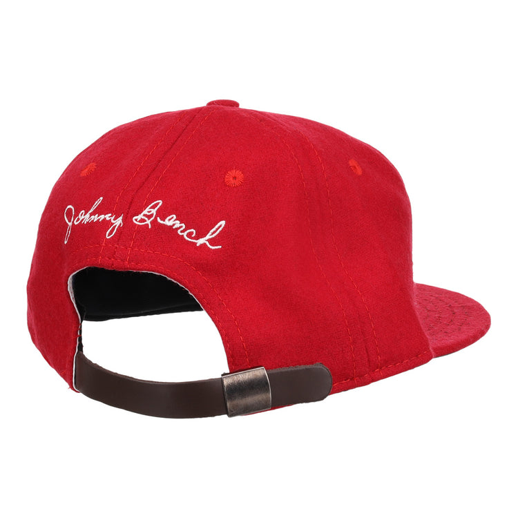 The Ebbets Field Flannels Johnny Bench Signature Series Ballcap is a red vintage wool cap with white embroidered cursive, inspired by Johnny Bench, and has an adjustable brown strap with a metal buckle at the back.