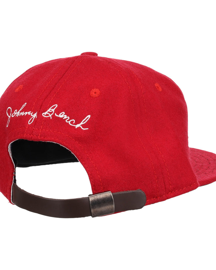 The Ebbets Field Flannels Johnny Bench Signature Series Ballcap is a red vintage wool cap with white embroidered cursive, inspired by Johnny Bench, and has an adjustable brown strap with a metal buckle at the back.