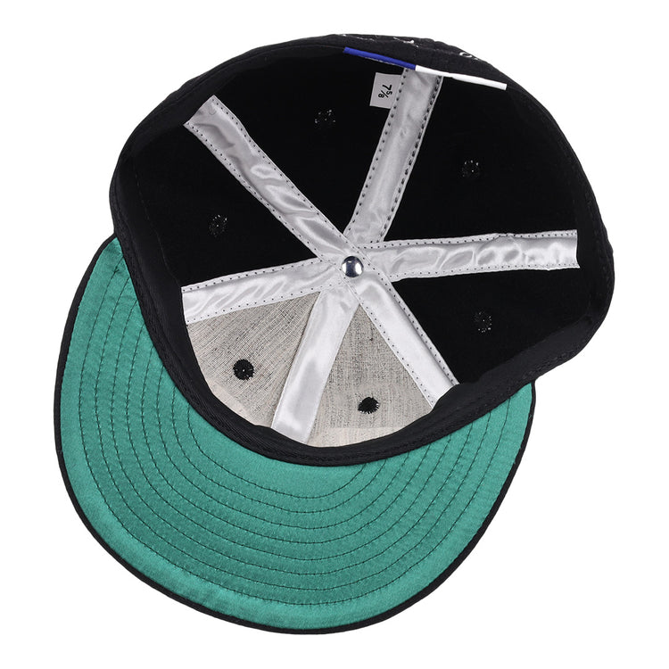 The image displays the inside of an Ebbets Field Flannels Monte Irvin Signature Series Ballcap, featuring a green underbrim, silver fabric lining, black rivets in the crown, and a white size tag—evoking early Negro National League styles.