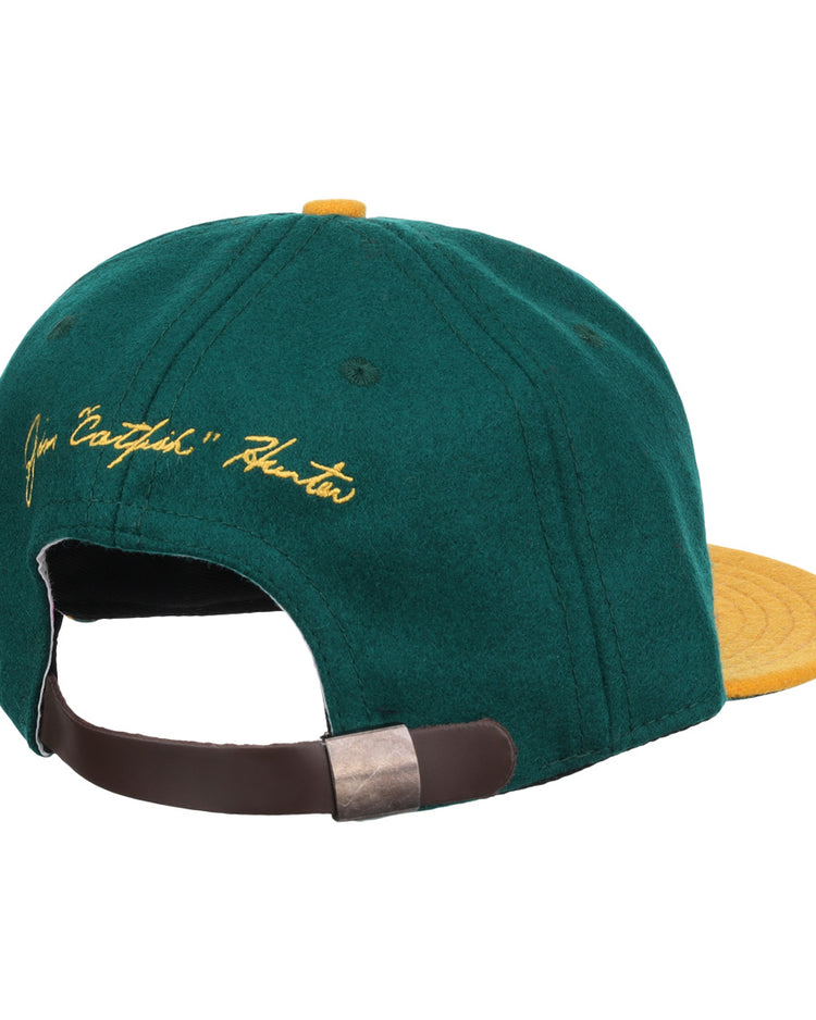 The Ebbets Field Flannels Catfish Hunter Signature Series Ballcap features vintage green wool, a yellow brim and button, yellow script embroidery on the back, and an adjustable brown strap with metal clasp.