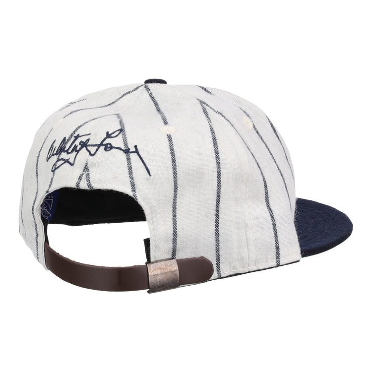 The Ebbets Field Flannels Whitey Ford Signature Series Ballcap features white fabric with dark pinstripes, a navy brim, an adjustable brown leather strap, and a black signature on the back for classic vintage style.