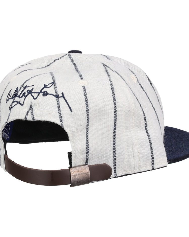 The Ebbets Field Flannels Whitey Ford Signature Series Ballcap features white fabric with dark pinstripes, a navy brim, an adjustable brown leather strap, and a black signature on the back for classic vintage style.