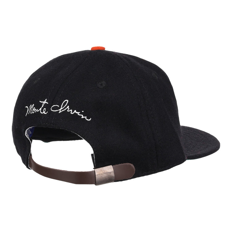 A black wool ballcap by Ebbets Field Flannels, the Monte Irvin Signature Series, shown from the back with an adjustable brown strap, metal clasp, and white cursive Monte Irvin above the opening—evoking classic Negro National League styles.