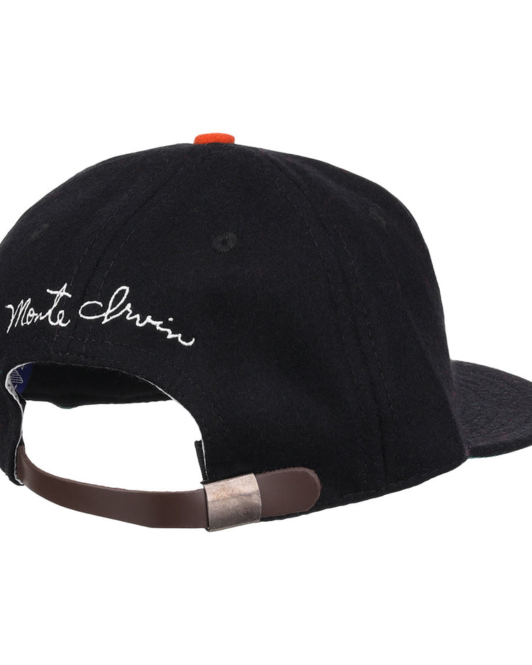 A black wool ballcap by Ebbets Field Flannels, the Monte Irvin Signature Series, shown from the back with an adjustable brown strap, metal clasp, and white cursive Monte Irvin above the opening—evoking classic Negro National League styles.