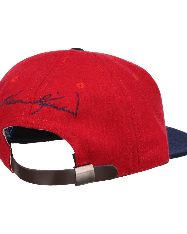 The Ebbets Field Flannels Harmon Killebrew Signature Series Ballcap, in red and navy vintage wool, is shown from the back with a brown adjustable strap, metal clasp, and black signature embroidery above the opening.